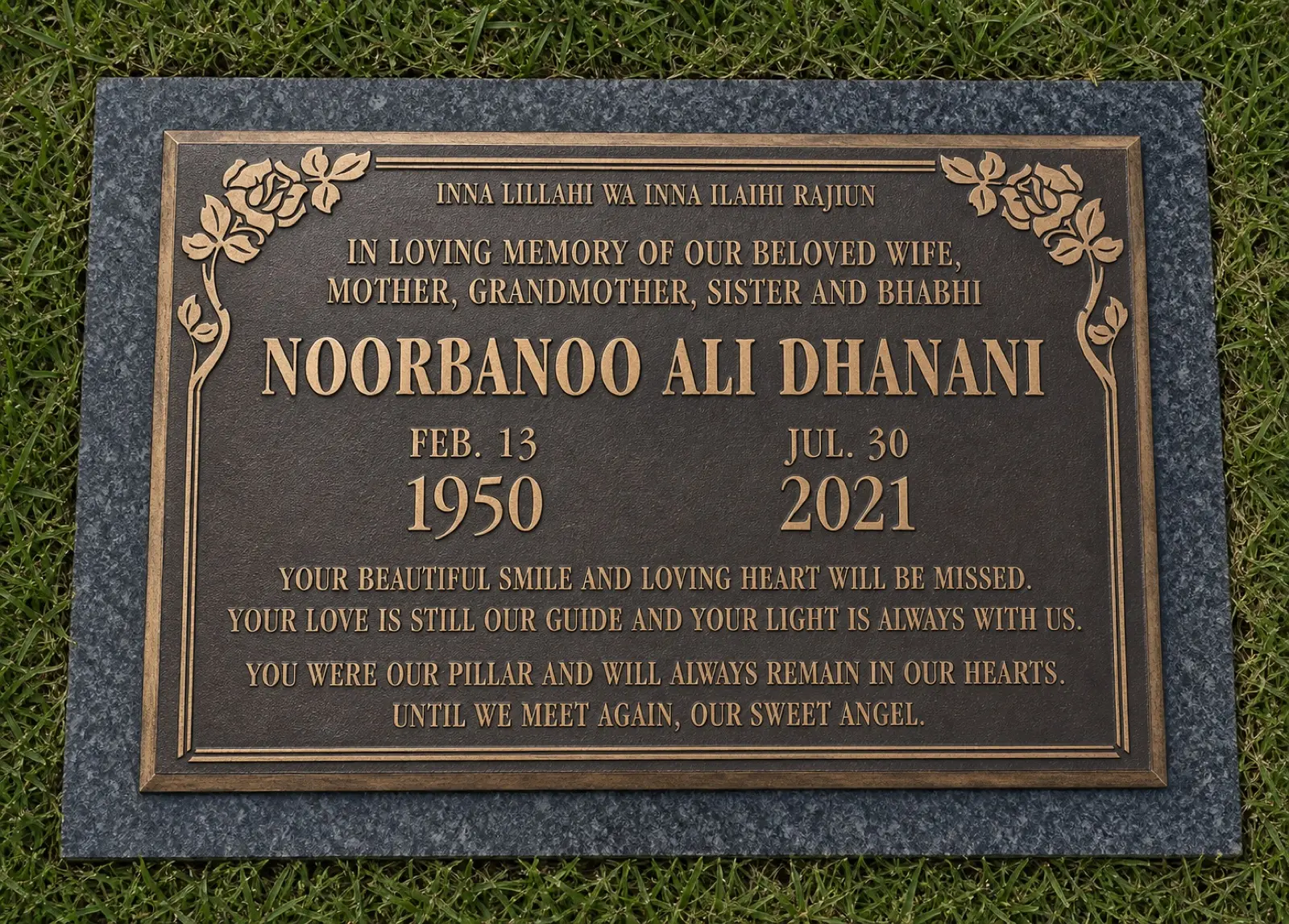 Realistic installed bronze memorial marker with multilingual lettering and rose artwork on granite and grass